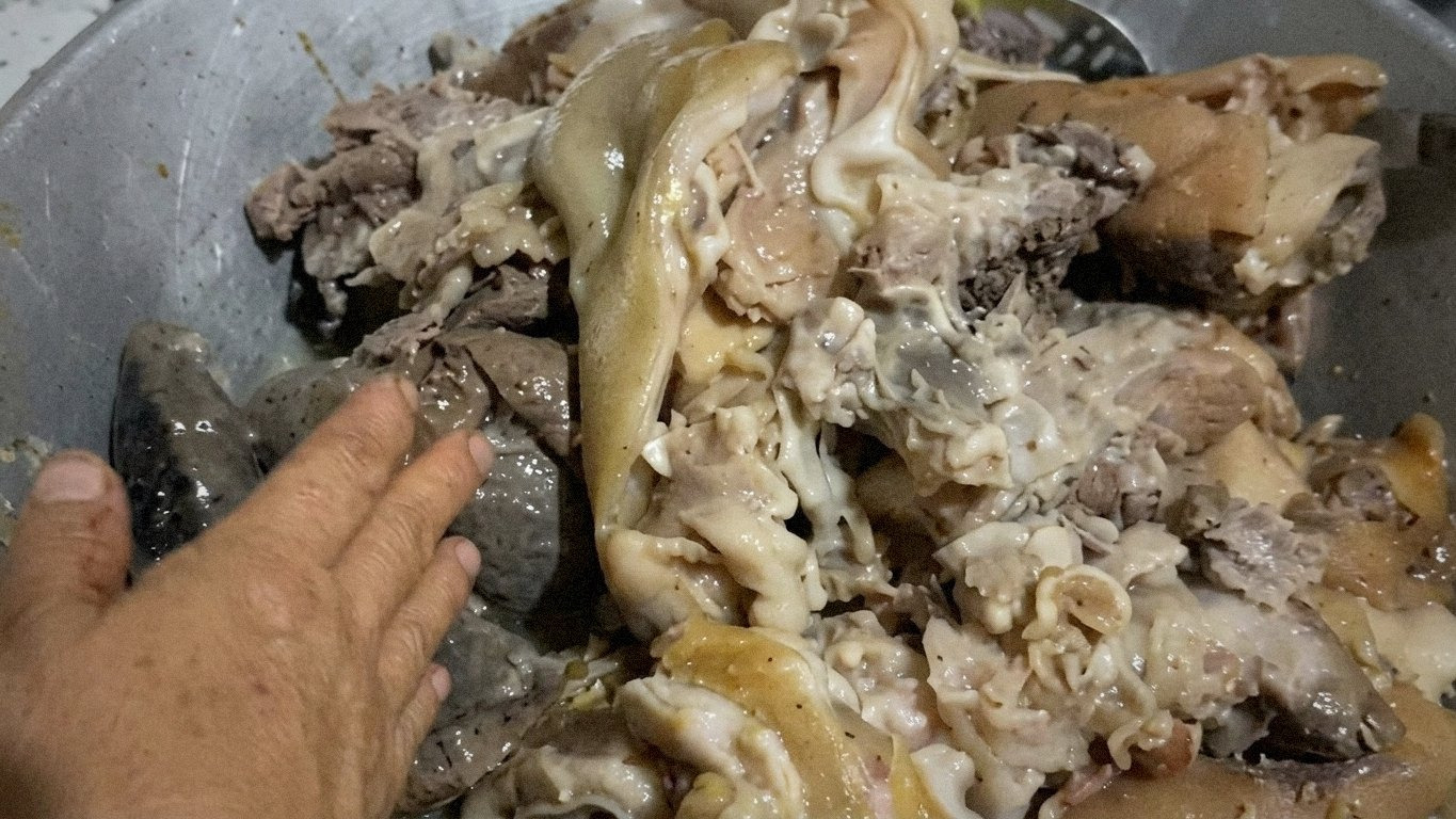 На плиті кипить каструля з вареним м'ясом, шматки свинячої голови та органів плавають у бульйоні.