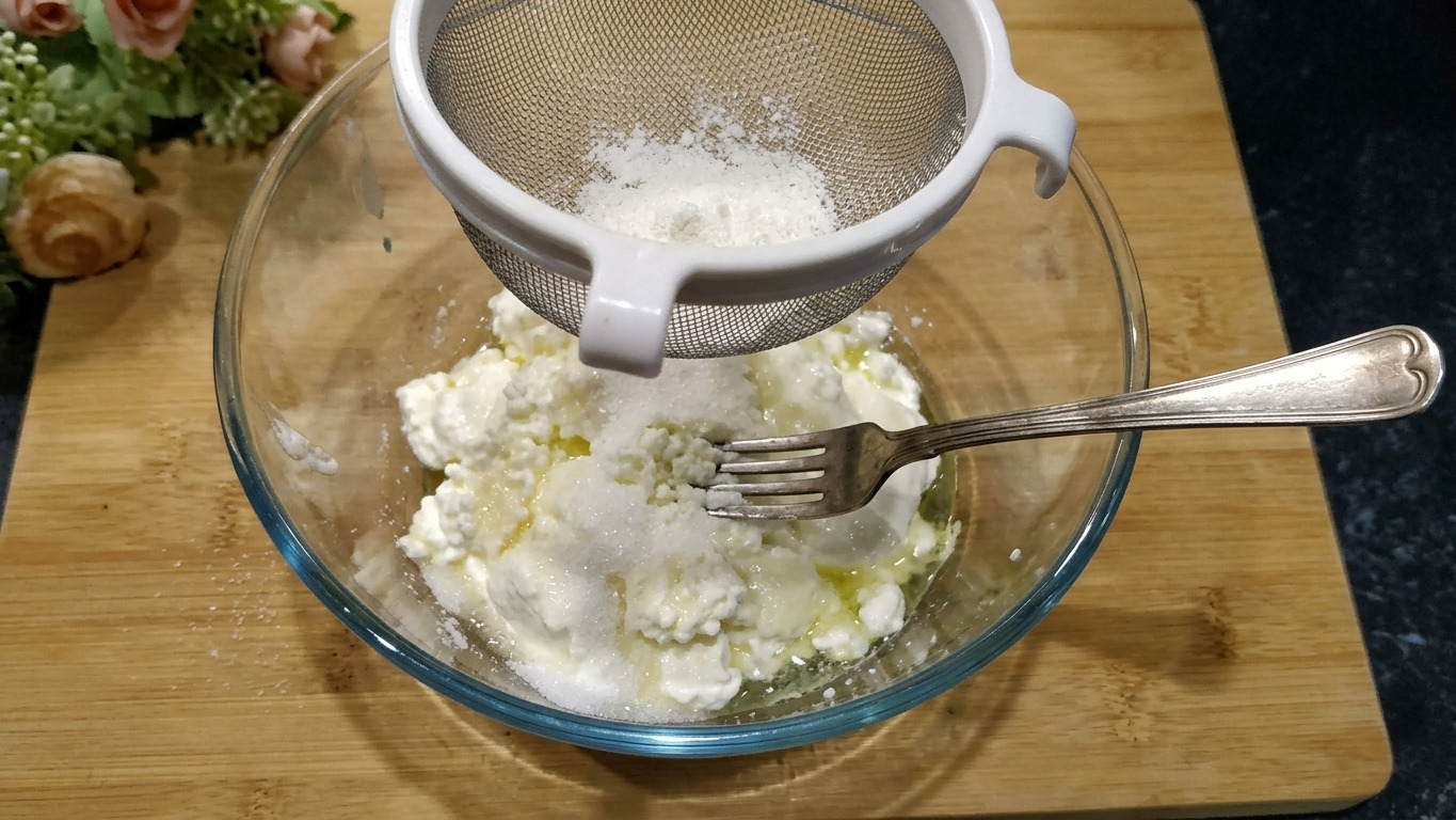 У мисці з творогом, цукром та сметаною, видно виделку для розминання.
